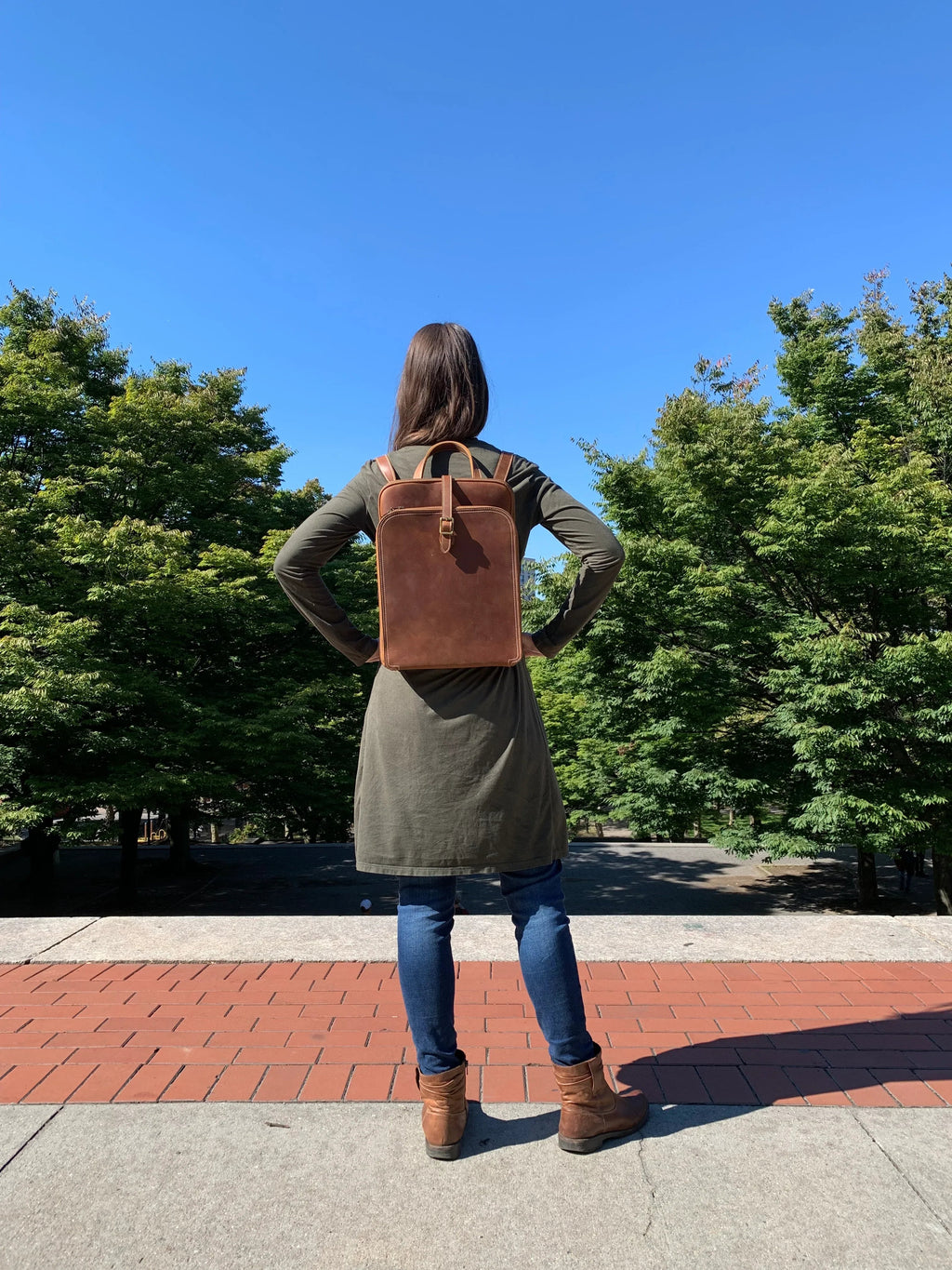 Person wearing a brown leather backpack outdoors on a sunny day
